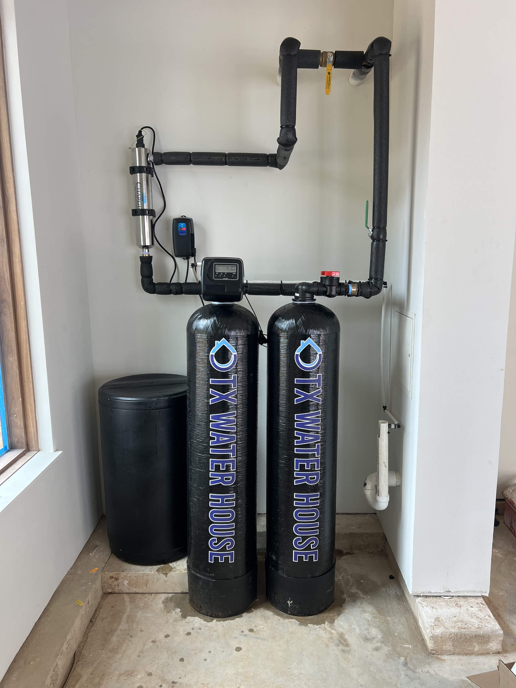 Two black water filtration systems with the Texas Water House logo on them, installed in a corner area of a home.