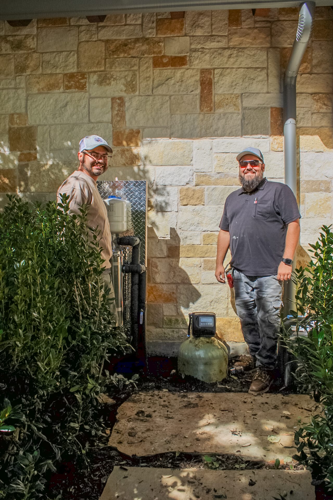 Two workers from Texas Water House standing outside next to a residential radon system.