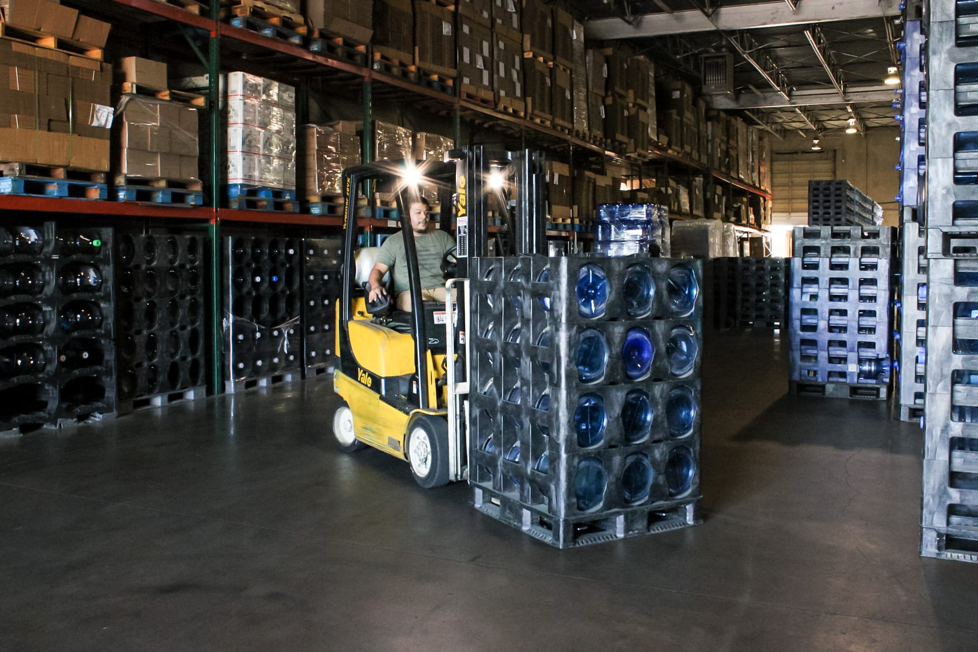 Dozens of full water jugs that are stored in Texas Water House's facility. Someone is moving a pallet with a lift.