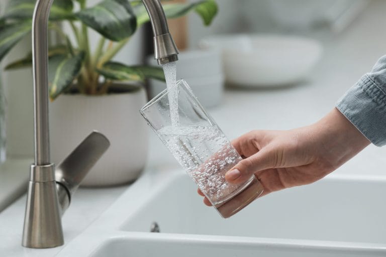 A person pours themselves a glass of water that's cleaner and clearer thanks to a water softener system.