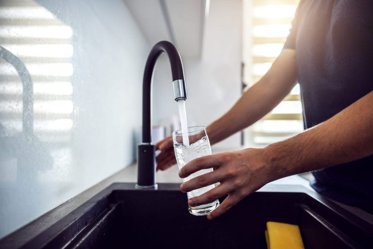 Stock image of a homeowner pouring a glass of water from the faucet. Hard water can affect drinking water.